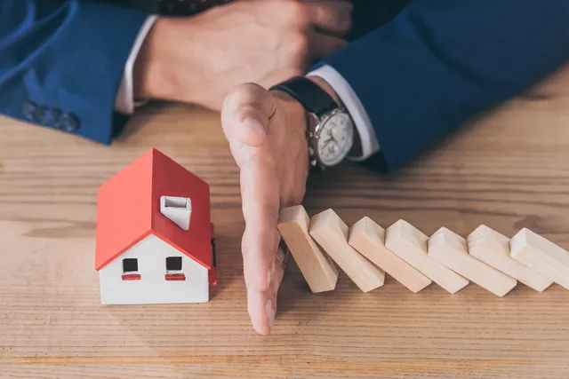Hands protecting a model house from falling dominoes