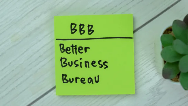 Green sticky note reading BBB Better Business Bureau on a pale wooden surface