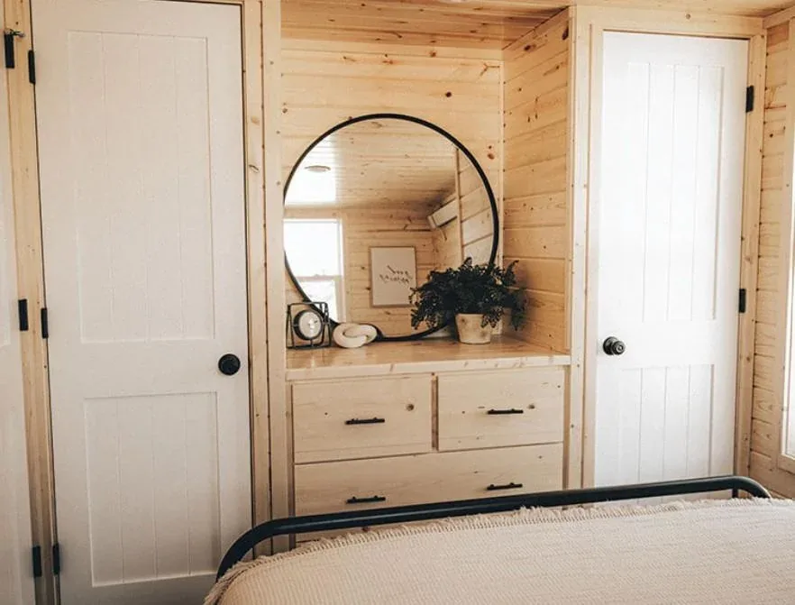 A tiny home bedroom with a round mirror and vanity
