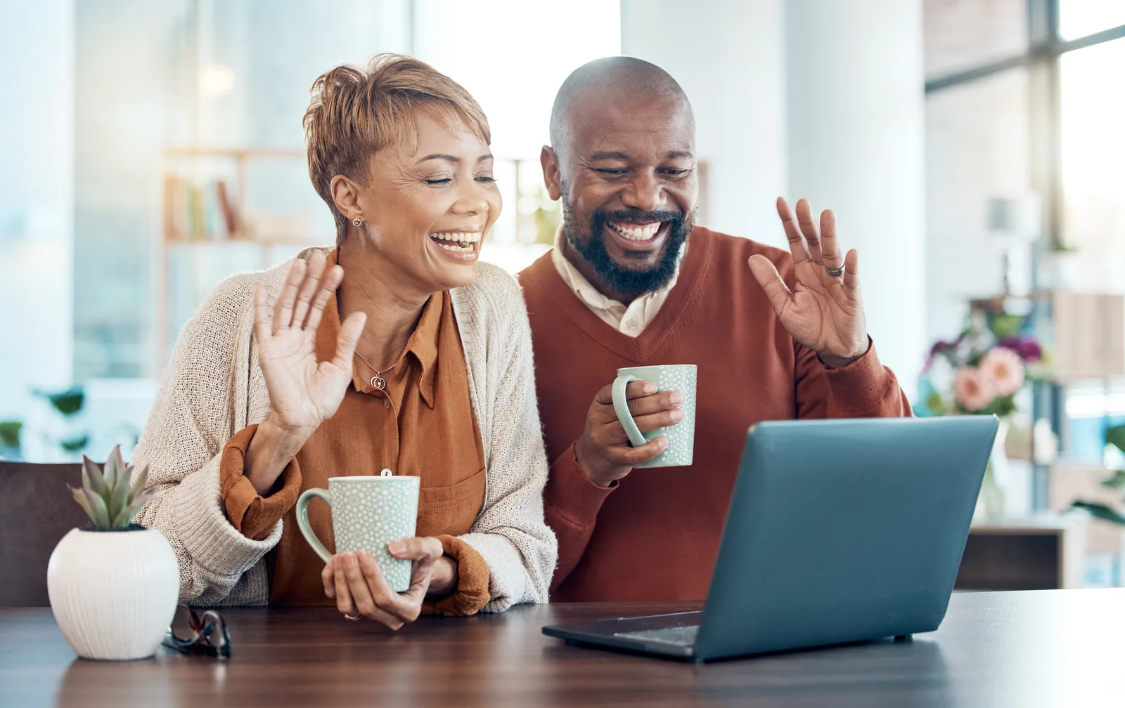 Couple smiling and waving during a video call on a laptop